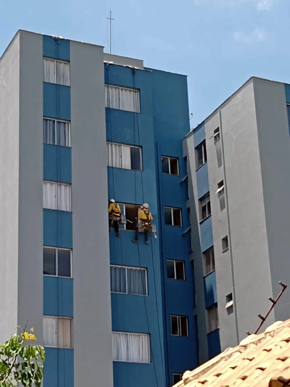 Técnicos pintando fachada de prédio por corda