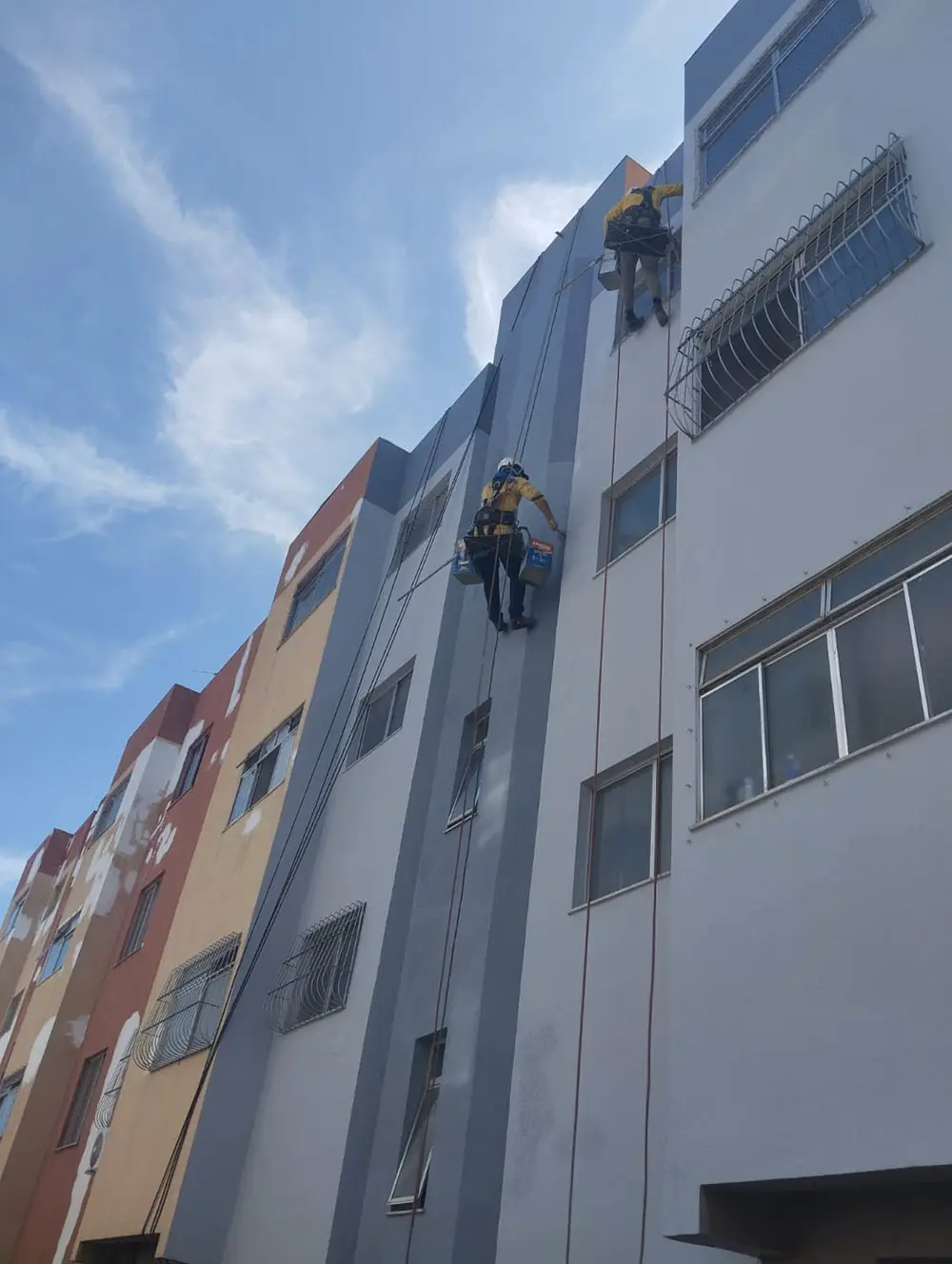 Técnicos em trabalho de altura pintando fachada